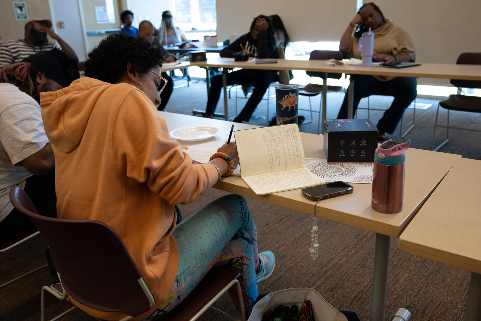 A woman writes in a journal beside a mandala coloring page and a new camera