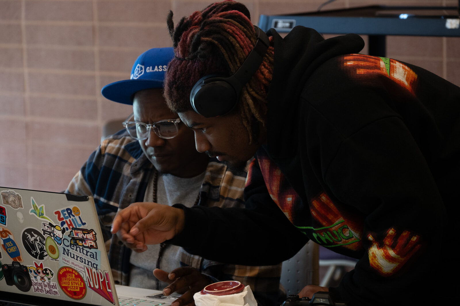 Two people review images together on a laptop covered in stickers